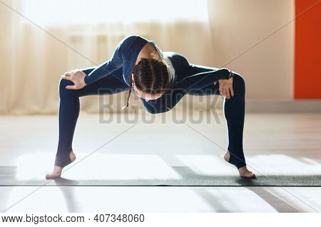 A Woman In Blue Sportswear Practicing Yoga, Performs Twisting In Rudrasana In An Apartment Near The 