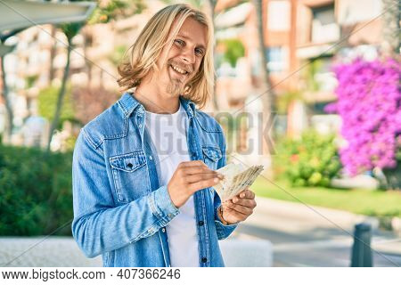 Young blond scandinavian man smiling happy counting danmark 100 kroner banknotes at the city.