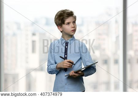Serious Little Boy With Tablet And Pen. Formal-dressed First Grader Is Writing Down Something On The