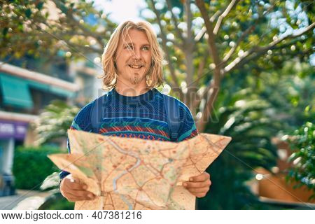 Young scandinavian tourist man smiling happy using map at the park.