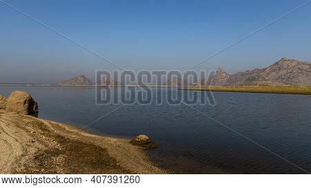 Landscape Of Jawai Dam With Water, Clear Blue Sky And Aravalli Mountain Ranges With Its Reflection I