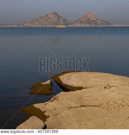 Landscape Of Jawai Dam With Water, Clear Blue Sky And Aravalli Mountain Ranges With Its Reflection I