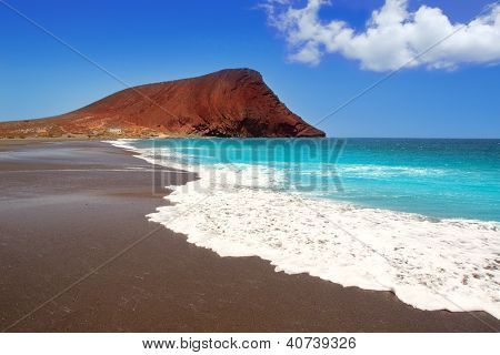 Stranden Playa de la Tejita turkos i Teneriffa Kanarieöarna med röda berg