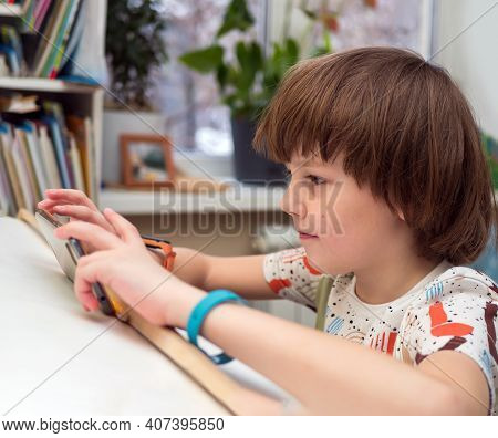 Eight Years Old Caucasian Boy In Casual Wear Is Using Smartphone At Home. Home Education Concept.