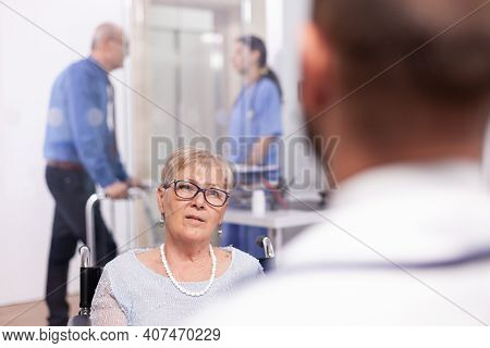 Disabled Old Person In Wheelchair During Treatment With Geriatrician Doctor. Medical Specialist Wear