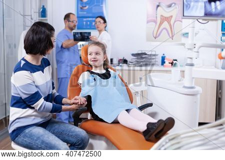 Little Girl Missing Milk Tooth Wearing Dental Bib Discussing With Parent At Dentist Consultation. Ch