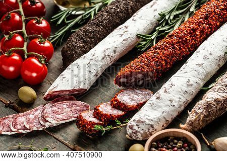 Variety Of Dry Cured Chorizo, Fuet And Other Sausages Cut In Slices With Herbs On Wooden Background.