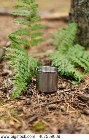 Enameled Tourist Mug In A Pine Forest On The Ground. The Atmosphere Of The Forest. Tea From A Thermo