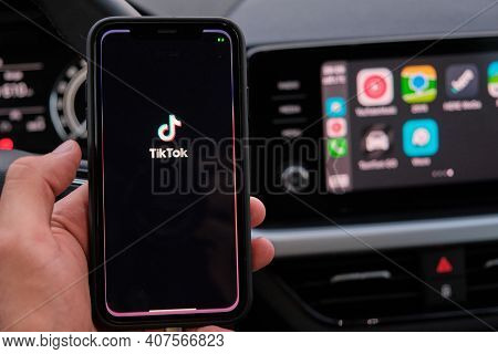 Tik Tok Logo On The Screen Of Smart Phone In Mans Hand On The Background Of Car Dashboard Screen Wit