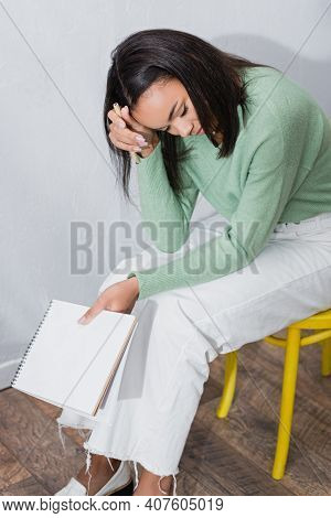 Exhausted African American Interior Designer Sitting On Chair With Blank Sketchbook.