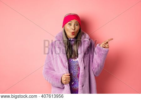 Cool Asian Granny Pointing Finger Right And Showing Promo Offer, Checking Out Special Deal On Pink B