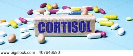 A Wooden Block With The Word Cortisol Stands On A Blue Background Among Multi-colored Pills. Medical