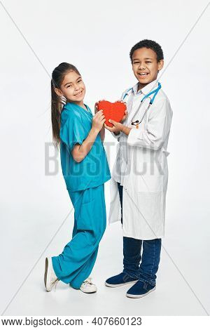Future Cardiac Doctors. Group Of Multiethnic Kids Wearing Medical Uniforms, Kids Hold Shape Of Heart