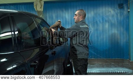 A Caucasian Man Works In A Car Wash Service. A Man In A Workers Uniform Is Wiping His Car With A Rag