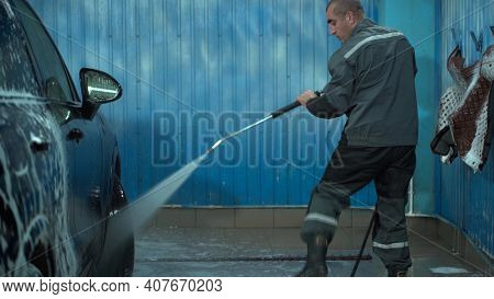 A Caucasian Man Works In A Car Wash Service. A Man In A Worker's Uniform Washes The Car Thoroughly B