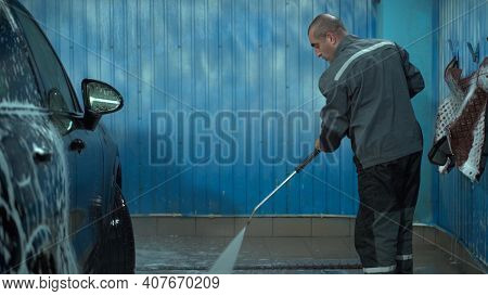 A Caucasian Man Works In A Car Wash Service. A Man In A Worker's Uniform Washes The Car Thoroughly B
