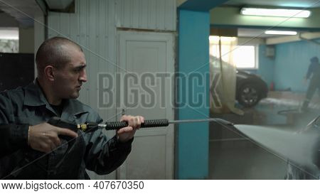 A Caucasian Man Works In A Car Wash Service. A Man In A Worker's Uniform Holds A Water Gun And Washe