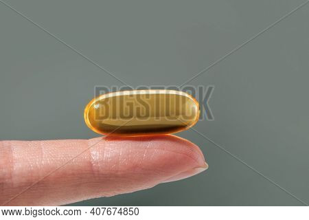 Female Hand Holding A Big Yellow Capsule Of Nutritional Supplement . Food Supplement, Vitamin D, Ome