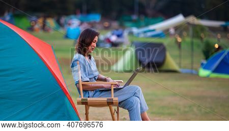 Female Traveler Sitting Beside Camping Tent And Using Notebook Laptop Computer Working With Other Te