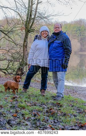 Multicultural Mature Married Couple Smiling At Camera By A Lake, Wearing Winter Clothes, Enjoying Na