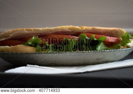 One Fresh Submarine Sandwich With Ham, Cheese, Tomatoes, Lettuce, Cucumbers In A Green Relief Plate