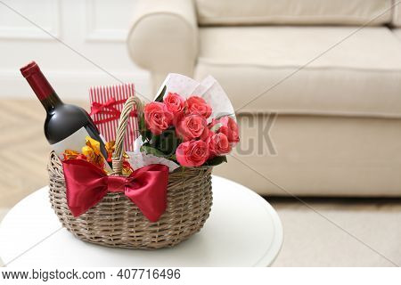 Wicker Basket With Gift, Bouquet And Wine On White Table Indoors. Space For Text