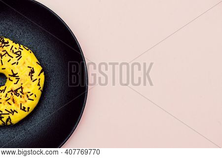 Half A Yellow Donut Decorated With Chocolate Sprinkles Isolated On Pink Background. Top View. Left S