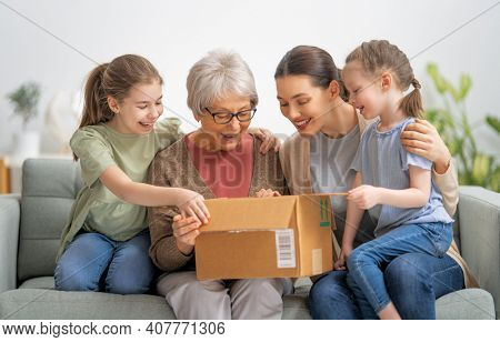 Grandmother, her daughter and granddaughters are unpacking cardboard box at home.