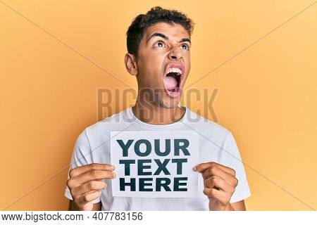 Young handsome african american man holding your text here banner angry and mad screaming frustrated and furious, shouting with anger looking up. 