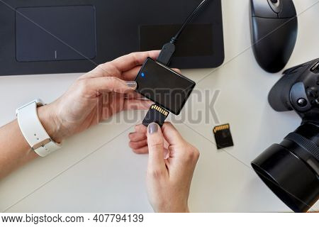 technology, post production and vlog concept - hands with sd memory card reader, digital camera and laptop computer working at office