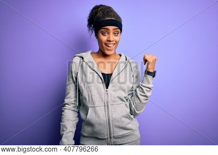 Young african american sportswoman doing sport wearing sportswear over purple background smiling with happy face looking and pointing to the side with thumb up.