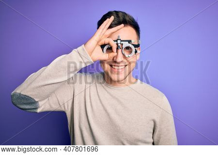Young handsome caucasian man wearing optometrical glasses over purple background doing ok gesture with hand smiling, eye looking through fingers with happy face.