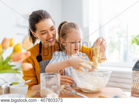 Happy loving family are preparing bakery together. Mother and child daughter girl are cooking cookies and having fun in the kitchen. Homemade food and little helper.     