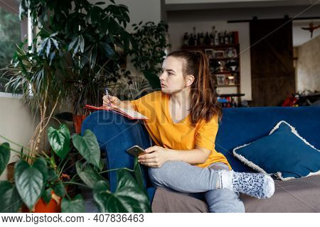 Satisfied And Happy Smiling Girl Sitting On The Sofa In The Room And Writes A Journal Of Your Dreams