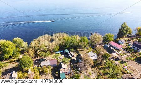Drone Fly Over Waving River Of Blue Color Surrounded By Local Village With Various Buildings And Wet