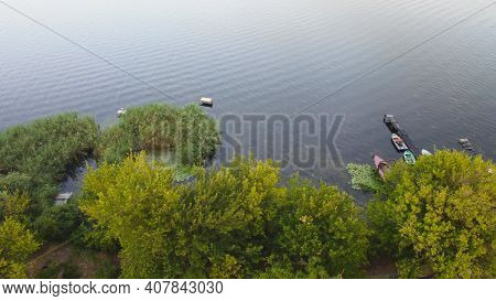 Drone Fly Over Waving River Of Blue Color Surrounded By Local Village With Various Buildings And Wet