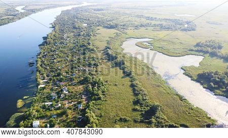 Drone Fly Over Waving River Of Blue Color Surrounded By Local Village With Various Buildings And Wet