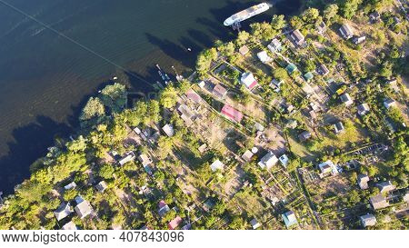 Drone Fly Over Waving River Of Blue Color Surrounded By Local Village With Various Buildings And Wet