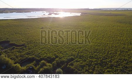 Drone Fly Over Waving River Of Blue Color Surrounded By Local Village With Various Buildings And Wet