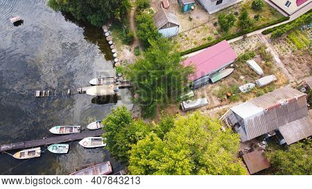 Drone Fly Over Waving River Of Blue Color Surrounded By Local Village With Various Buildings And Wet
