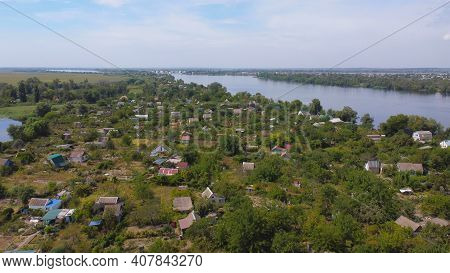 Drone Fly Over Waving River Of Blue Color Surrounded By Local Village With Various Buildings And Wet