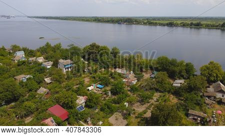 Drone Fly Over Waving River Of Blue Color Surrounded By Local Village With Various Buildings And Wet