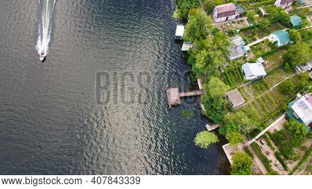 Drone Fly Over Waving River Of Blue Color Surrounded By Local Village With Various Buildings And Wet