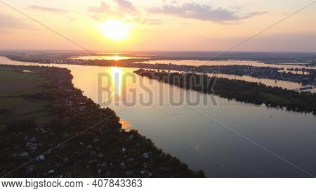 Drone Fly Over Waving River Of Blue Color Surrounded By Local Village With Various Buildings And Wet