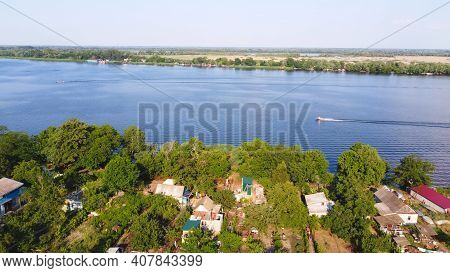 Drone Fly Over Waving River Of Blue Color Surrounded By Local Village With Various Buildings And Wet