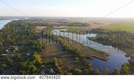Drone Fly Over Waving River Of Blue Color Surrounded By Local Village With Various Buildings And Wet