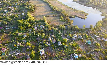 Drone Fly Over Waving River Of Blue Color Surrounded By Local Village With Various Buildings And Wet