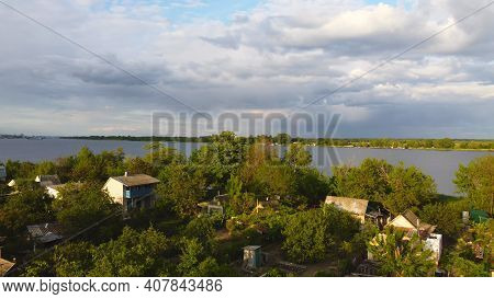 Drone Fly Over Waving River Of Blue Color Surrounded By Local Village With Various Buildings And Wet