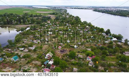 Drone Fly Over Waving River Of Blue Color Surrounded By Local Village With Various Buildings And Wet