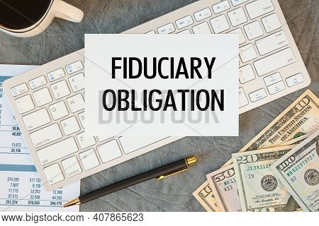 Fiduciary Obligation Is Written In A Document On The Office Desk With Office Accessories, Coffee, Mo